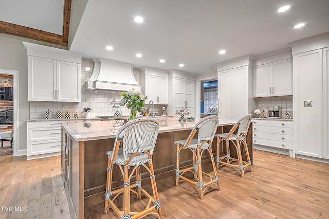 kitchen featuring a kitchen island with sink, white cabinets, and premium range hood