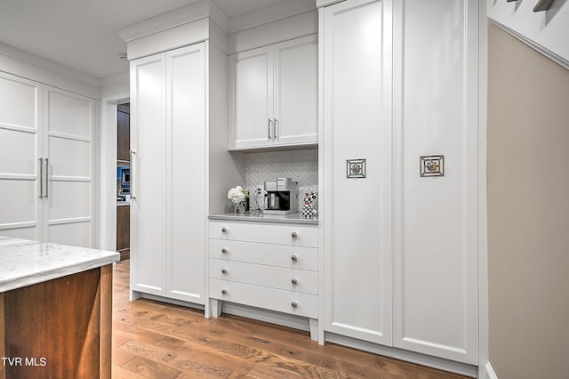 kitchen with white cabinetry, wood-type flooring, light stone countertops, and backsplash