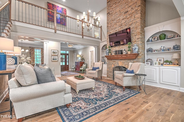 living room featuring an inviting chandelier, light hardwood / wood-style flooring, built in features, a fireplace, and a high ceiling