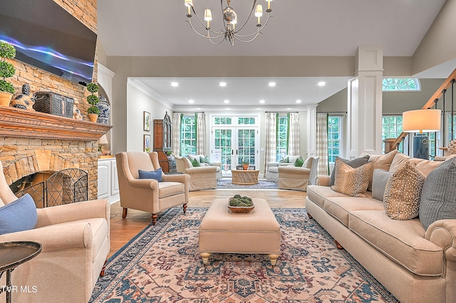 living room with crown molding, light hardwood / wood-style flooring, an inviting chandelier, decorative columns, and a fireplace