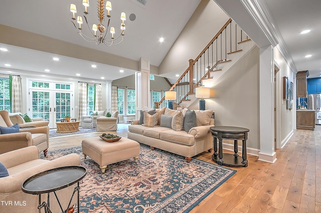 living room with french doors, ornate columns, an inviting chandelier, light wood-type flooring, and ornamental molding