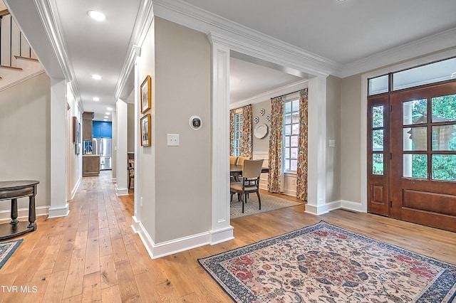 foyer with crown molding, decorative columns, and light wood-type flooring