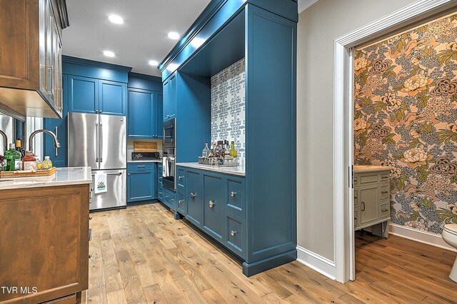 kitchen featuring blue cabinetry, appliances with stainless steel finishes, crown molding, and light hardwood / wood-style floors