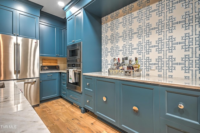 kitchen featuring stainless steel appliances, light stone countertops, blue cabinetry, and light hardwood / wood-style floors