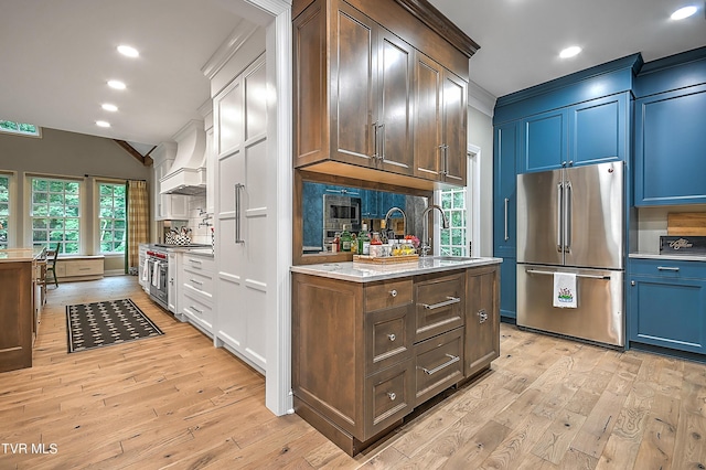 kitchen with stainless steel appliances, premium range hood, sink, and light wood-type flooring