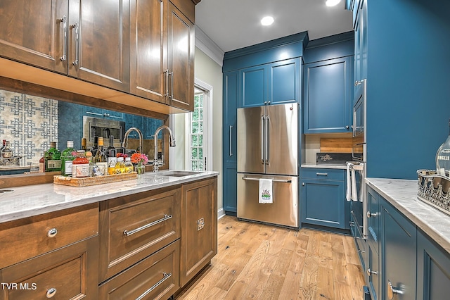 kitchen with sink, light stone counters, crown molding, light wood-type flooring, and appliances with stainless steel finishes