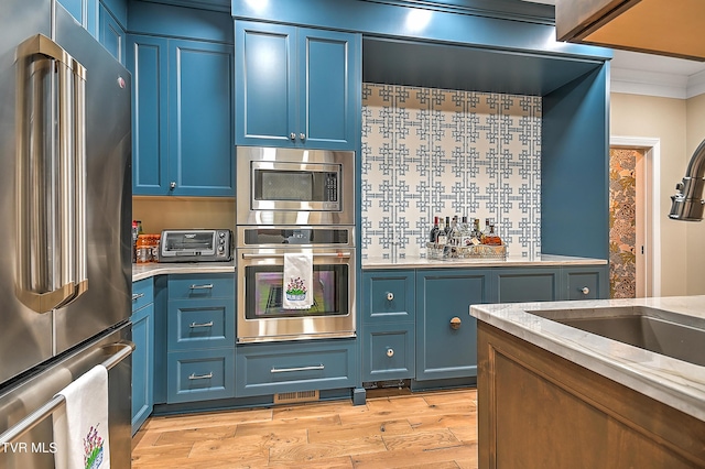 kitchen featuring appliances with stainless steel finishes, blue cabinetry, and light hardwood / wood-style flooring