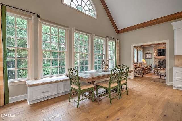 dining room featuring plenty of natural light, a fireplace, high vaulted ceiling, and light hardwood / wood-style flooring