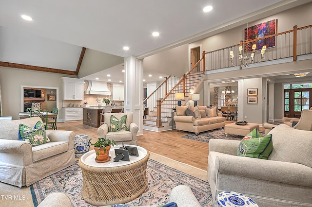 living room with an inviting chandelier, high vaulted ceiling, decorative columns, and light wood-type flooring