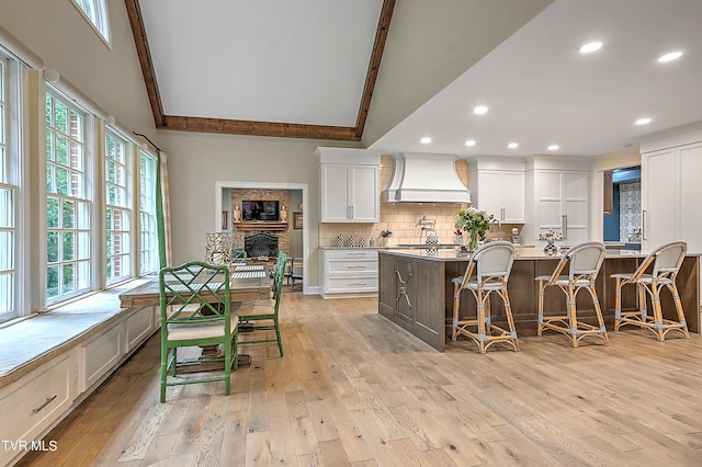 kitchen featuring premium range hood, light stone counters, a kitchen breakfast bar, a kitchen island with sink, and white cabinets