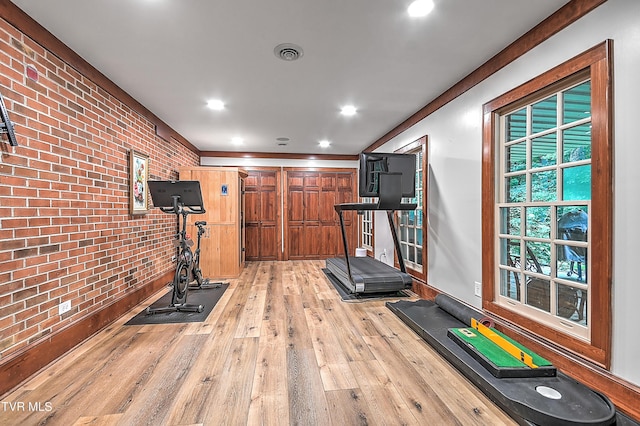 exercise area with light hardwood / wood-style flooring and brick wall