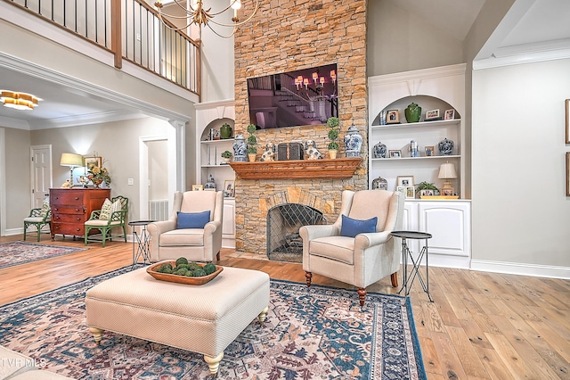 living room featuring built in shelves, ornamental molding, a chandelier, and light wood-type flooring