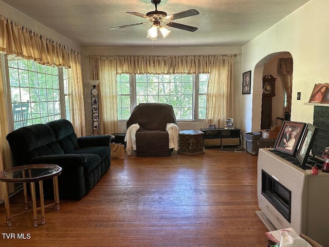 living room featuring ceiling fan, wood-type flooring, a textured ceiling, and a fireplace