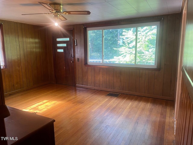 spare room featuring wooden walls, visible vents, baseboards, a ceiling fan, and light wood finished floors