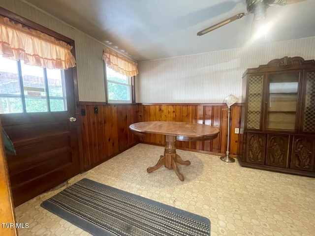 dining room with ceiling fan, wainscoting, wood walls, and wallpapered walls