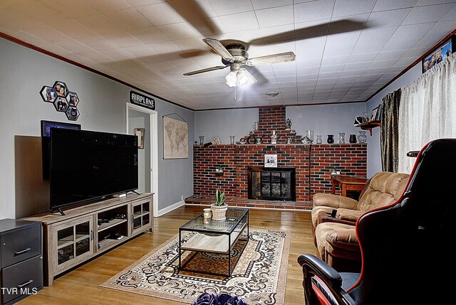 living room with a fireplace, light wood-type flooring, crown molding, and ceiling fan