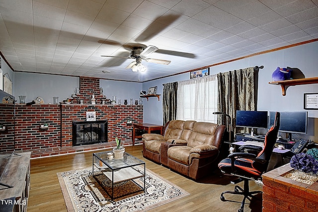 living room with light wood-type flooring, ornamental molding, ceiling fan, and a brick fireplace