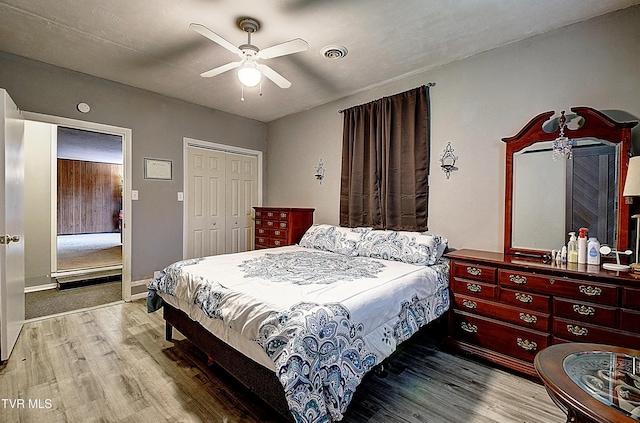 bedroom with a ceiling fan, wood finished floors, visible vents, baseboards, and a closet