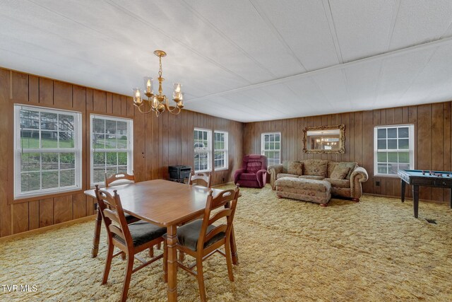 carpeted dining room with wood walls and a notable chandelier