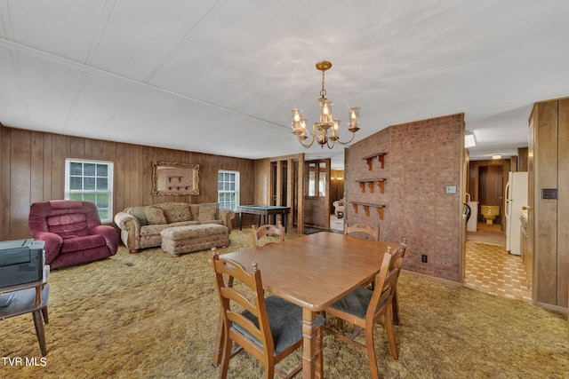 carpeted dining space with wood walls, an inviting chandelier, and brick wall