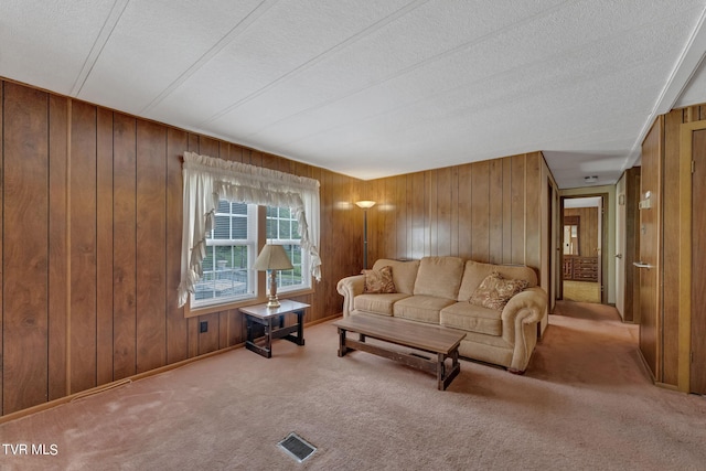 living room with light carpet, wood walls, a textured ceiling, and visible vents