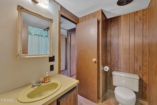 full bathroom featuring toilet, wood walls, a textured ceiling, and vanity