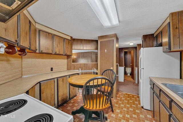 kitchen featuring brown cabinets, light countertops, wood walls, a sink, and white appliances