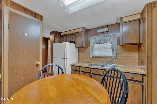 kitchen with light countertops, brown cabinetry, freestanding refrigerator, a sink, and a textured ceiling