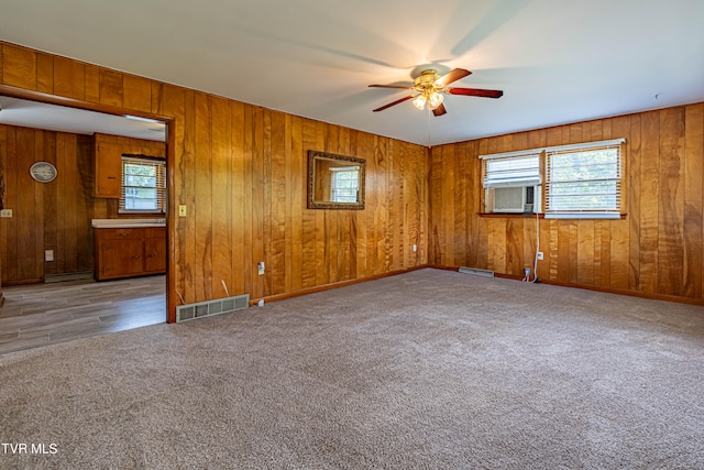 carpeted spare room featuring a wealth of natural light, wooden walls, and ceiling fan