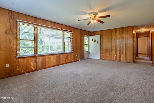 empty room featuring carpet, wooden walls, a wealth of natural light, and ceiling fan