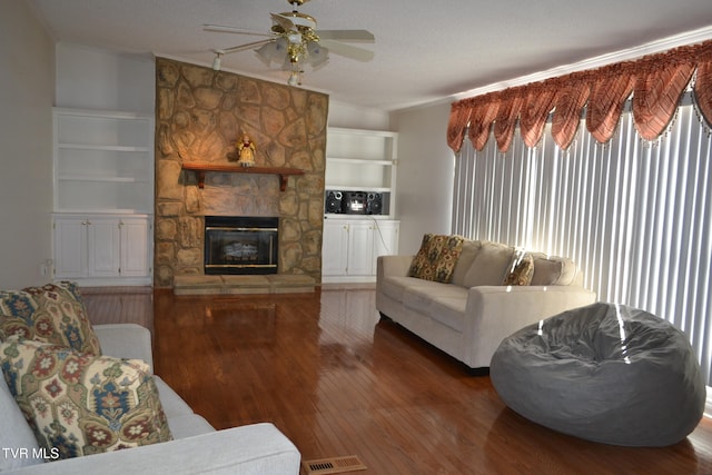 living room featuring built in shelves, a fireplace, a textured ceiling, and hardwood / wood-style flooring