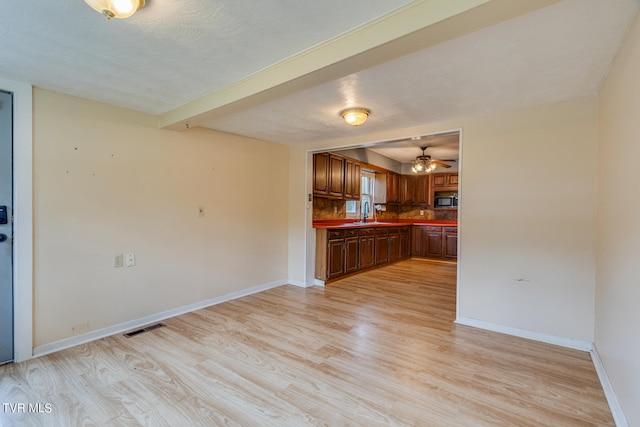 unfurnished living room featuring light wood-type flooring, sink, ceiling fan, and beamed ceiling