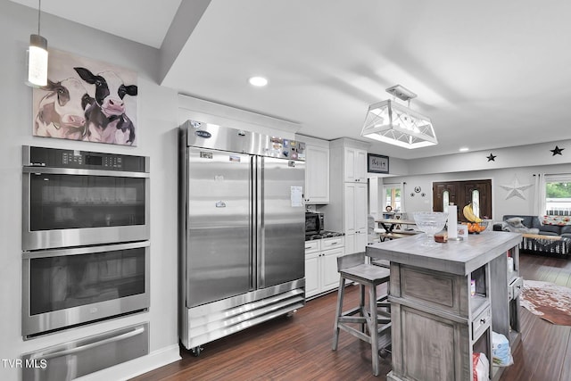 kitchen featuring white cabinets, appliances with stainless steel finishes, a warming drawer, dark wood finished floors, and decorative light fixtures