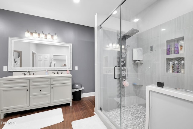 bathroom featuring double vanity, wood finished floors, a sink, and a shower stall