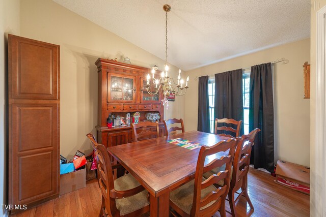 dining room with a textured ceiling, lofted ceiling, a chandelier, and wood-type flooring