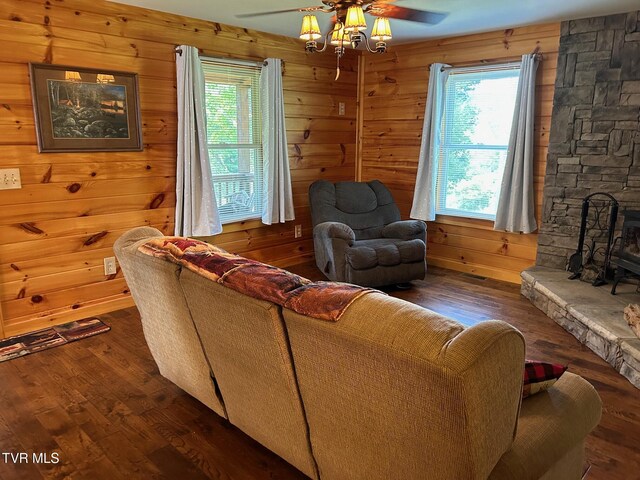 living room featuring ceiling fan, a fireplace, wood walls, and dark wood-type flooring