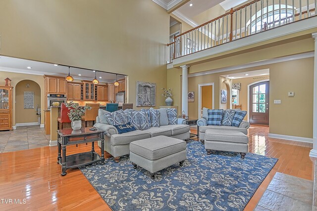 living room with decorative columns, ornamental molding, a towering ceiling, and light hardwood / wood-style flooring