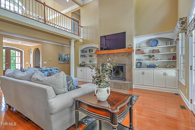 living room featuring crown molding, hardwood / wood-style floors, a towering ceiling, a fireplace, and built in shelves