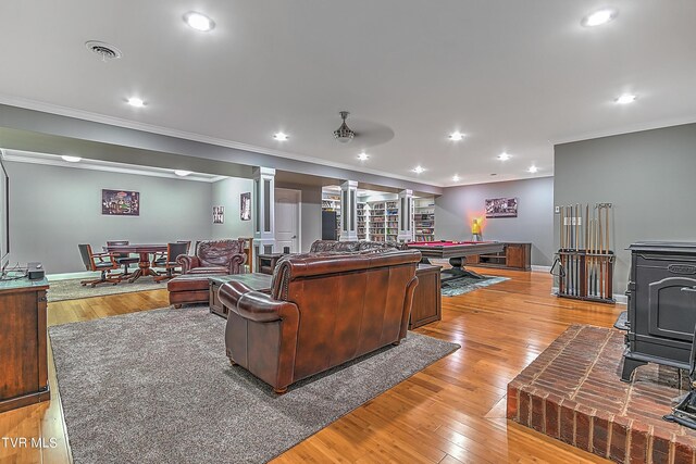 living room featuring billiards, ornamental molding, light hardwood / wood-style floors, and a wood stove