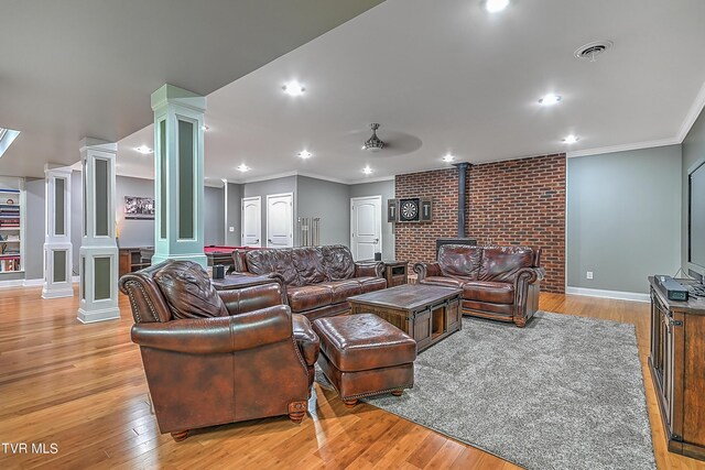 living room featuring ornate columns, crown molding, a wood stove, and light wood-type flooring