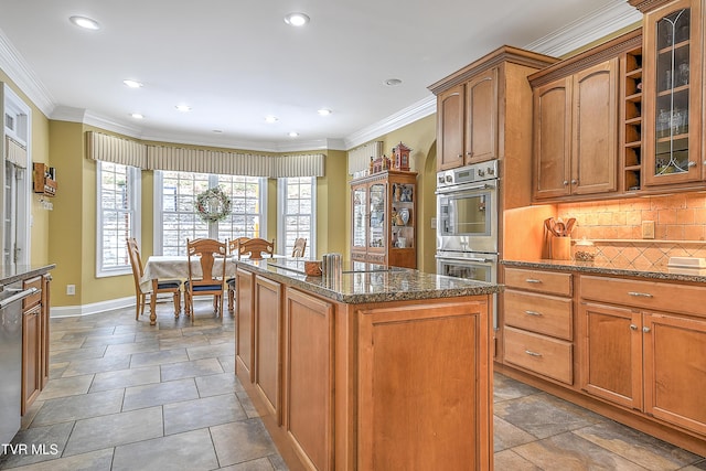 kitchen featuring stainless steel appliances, a center island, ornamental molding, dark stone counters, and backsplash