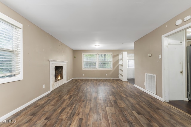 unfurnished living room with dark wood-type flooring and a brick fireplace