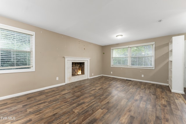 unfurnished living room with dark hardwood / wood-style flooring and a brick fireplace