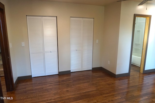 unfurnished bedroom featuring ceiling fan, connected bathroom, dark hardwood / wood-style flooring, and multiple closets