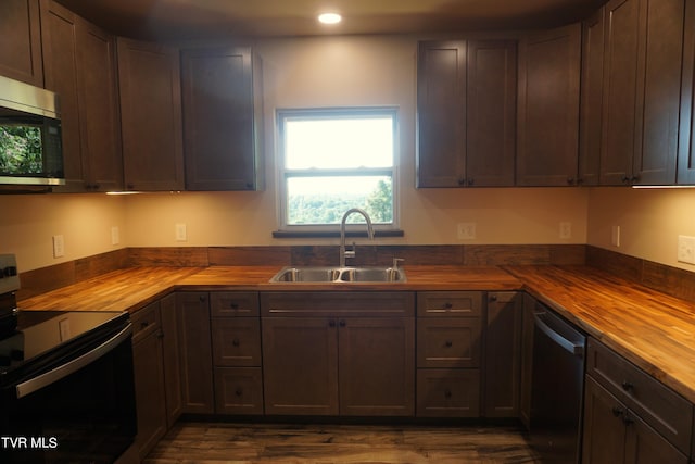 kitchen featuring stainless steel appliances, sink, dark brown cabinets, wooden counters, and dark wood-type flooring