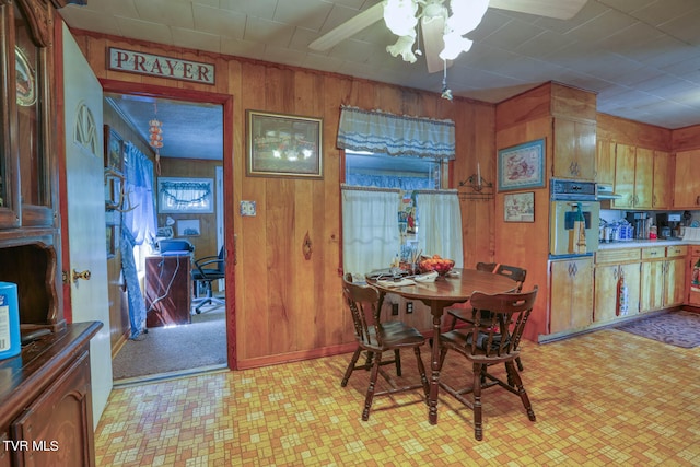 dining area featuring ceiling fan, wood walls, and light colored carpet