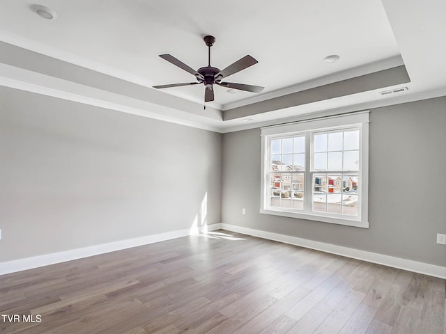 unfurnished room featuring a raised ceiling, ceiling fan, ornamental molding, and light wood-type flooring