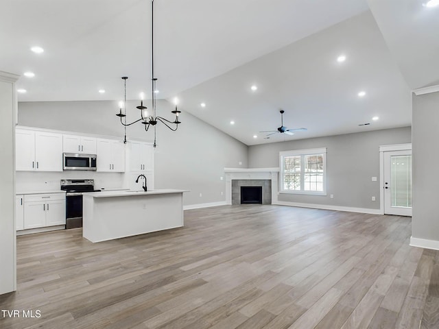 kitchen with white cabinetry, stainless steel appliances, pendant lighting, a center island with sink, and ceiling fan with notable chandelier