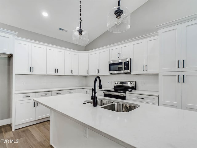 kitchen featuring lofted ceiling, white cabinets, hanging light fixtures, appliances with stainless steel finishes, and tasteful backsplash