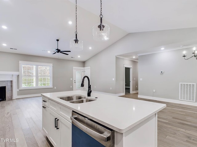 kitchen with stainless steel dishwasher, sink, a center island with sink, white cabinets, and hanging light fixtures